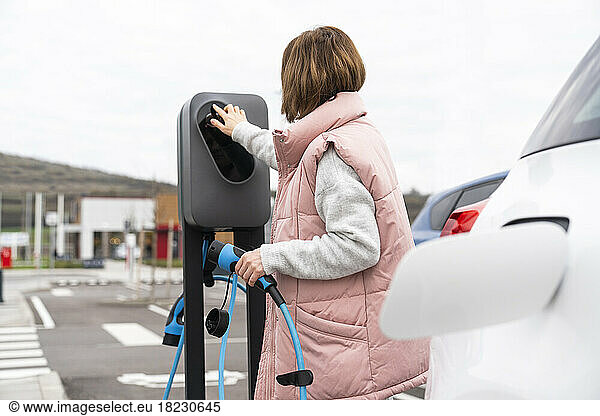Woman operating kiosk holding charger at station