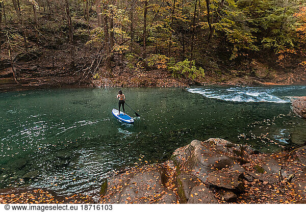 Woman paddle boarding in a fall scene on a clear river