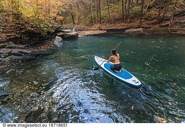 Woman paddle boarding in a fall scene on a clear river