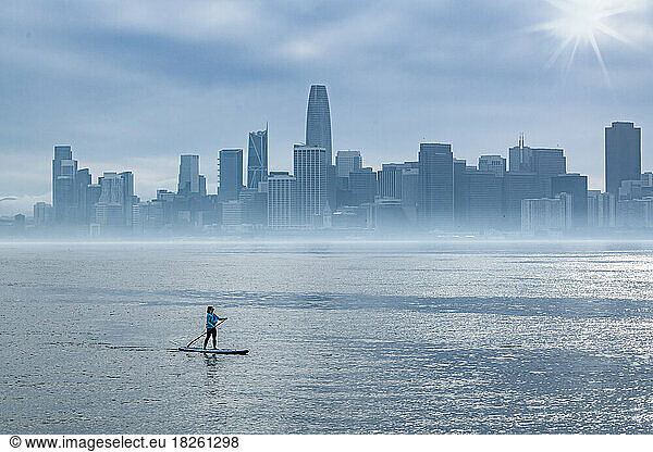 Woman paddleboarding in bay while city skyline in background