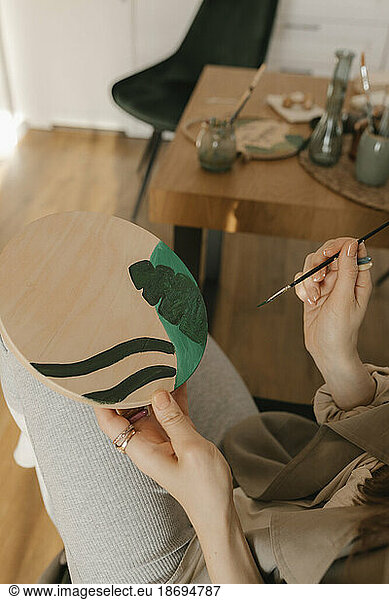 Woman painting on wooden board sitting by table