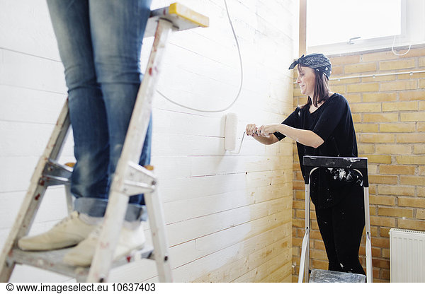 Woman painting wooden wall with paint roller