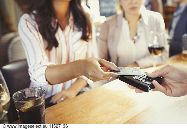 Woman paying bartender with credit card contactless payment at bar