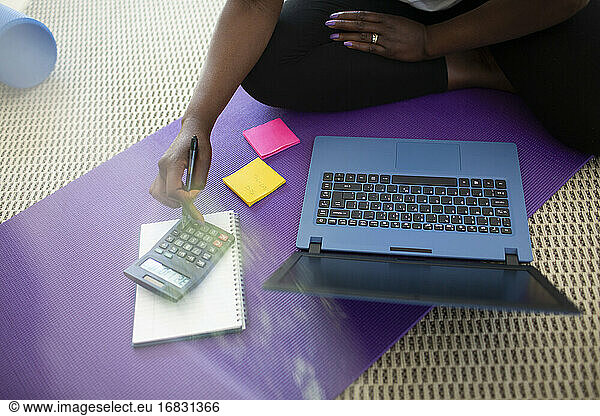 Woman paying bills at laptop on yoga mat at home