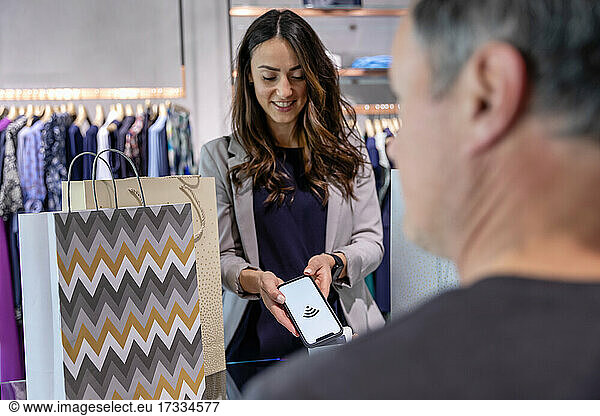 Woman paying contactless through smart phone at clothes store