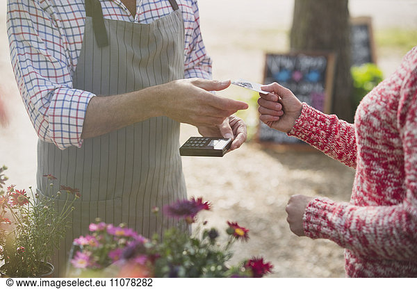 Woman paying plant nursery worker with credit card