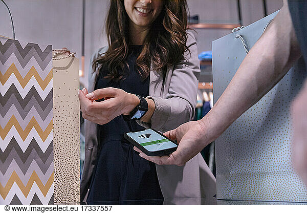 Woman paying through smart watch near mobile phone at clothes store