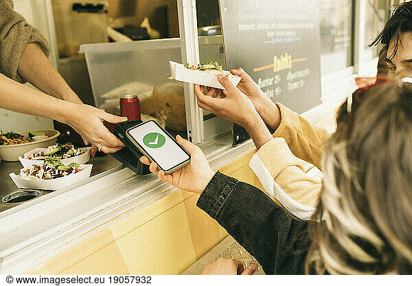 Woman paying via tap to pay method through smart phone while buying food from concession stand