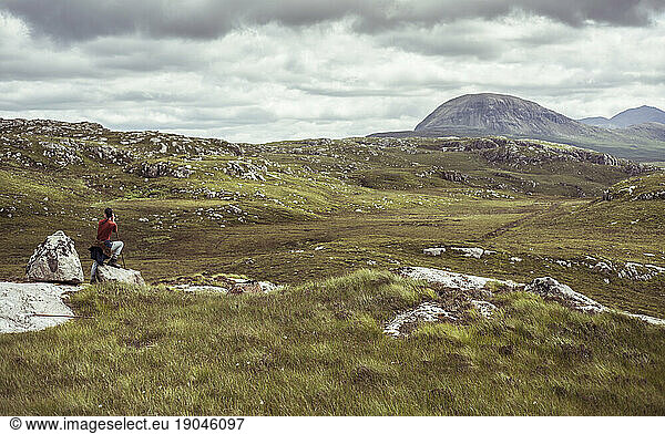 Woman perched on rock in Scottish landscape looking with binoculars