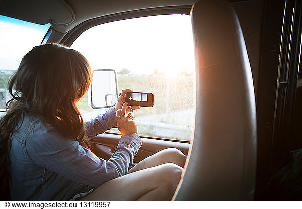 Woman photographing by window while travelling in camper van
