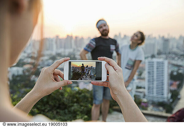 Woman photographing couple with smart phone at sunset in city