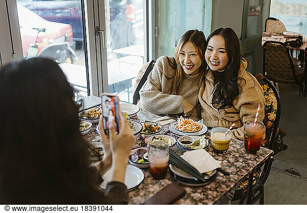 Woman photographing female friends sitting with food at restaurant
