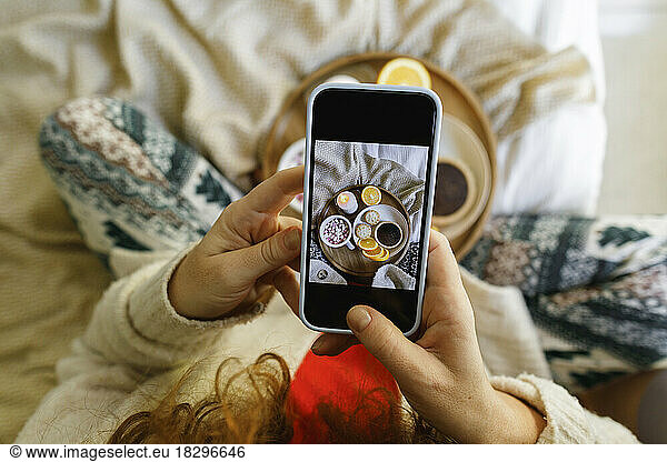 Woman photographing food through smart phone on bed at home