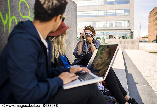 Woman photographing freelancers while sitting by wall