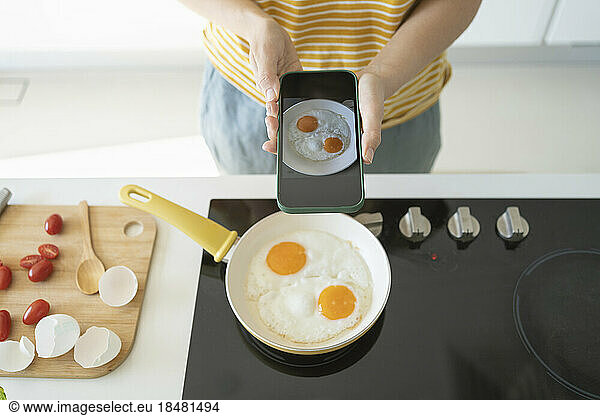 Woman photographing fried eggs with smart phone at home