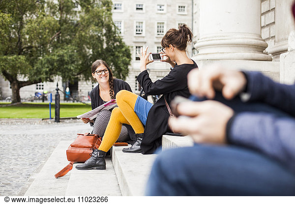 Woman photographing friend while sitting on steps