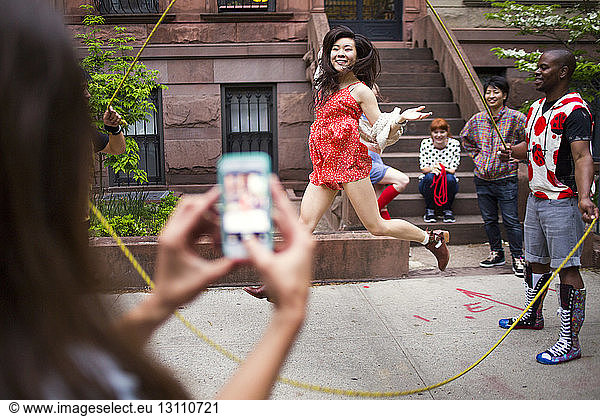 Woman photographing friends performing double Dutch on sidewalk