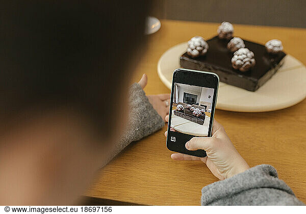 Woman photographing homemade cake with smart phone at home