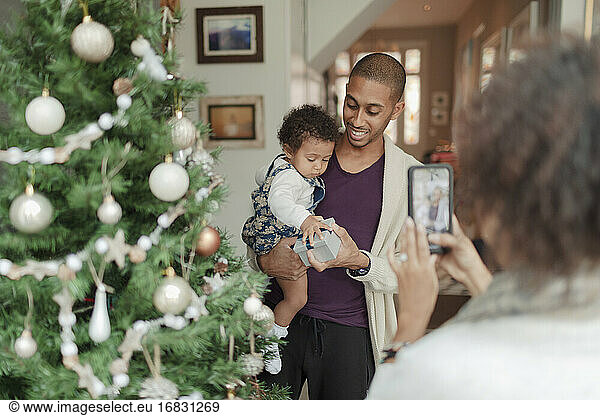 Woman photographing husband and baby daughter at Christmas tree