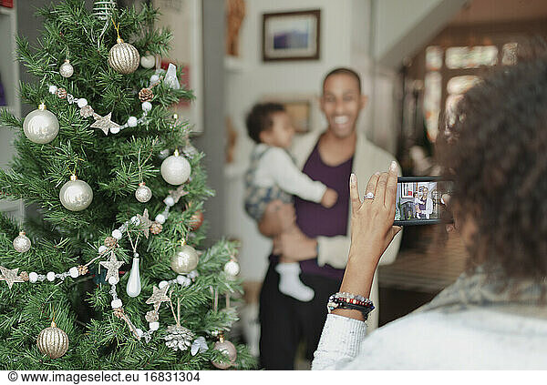 Woman photographing husband and baby daughter by Christmas tree