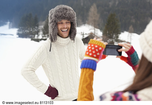 Woman photographing man in fur hat in snowy field