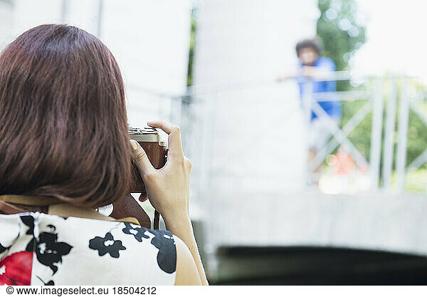 Woman photographing man standing on bridge