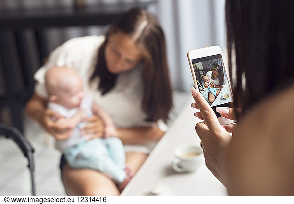 Woman photographing mother with baby son (2-5 months) in cafe