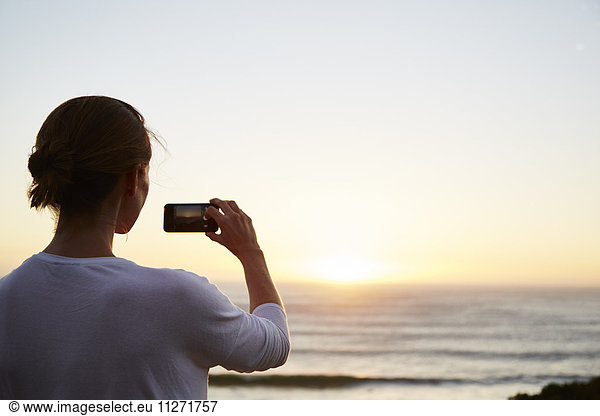 Woman photographing sunset over ocean with camera phone