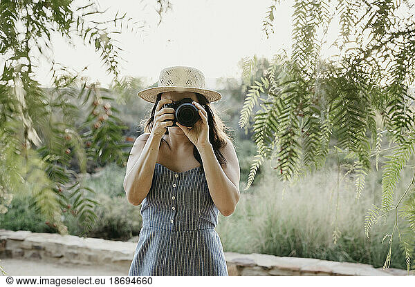 Woman photographing through camera standing near plants