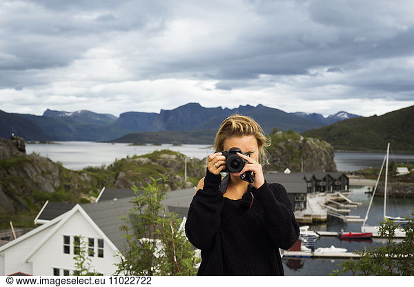 Woman photographing through digital camera against mountains