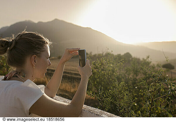 Woman photographing through smart phone at sunset
