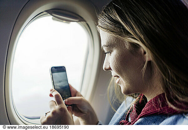 Woman photographing through smart phone in airplane