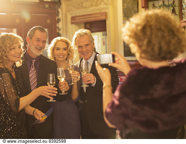Woman photographing well dressed couples toasting champagne glasses in theater lobby