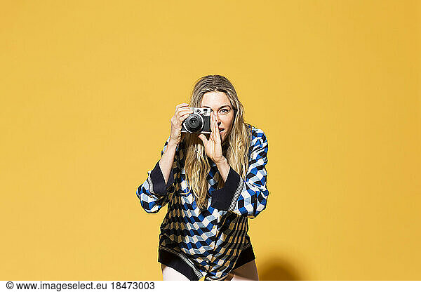 Woman photographing with camera against yellow background