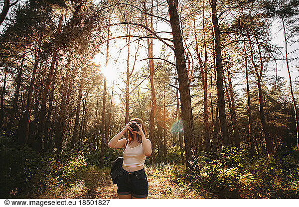 Woman photographing with camera in forest during summer