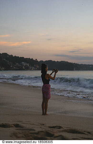 Woman photographs a sunset on the ocean with a camera.