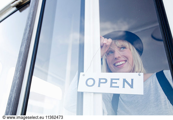 Woman placing open sign on glass door smiling