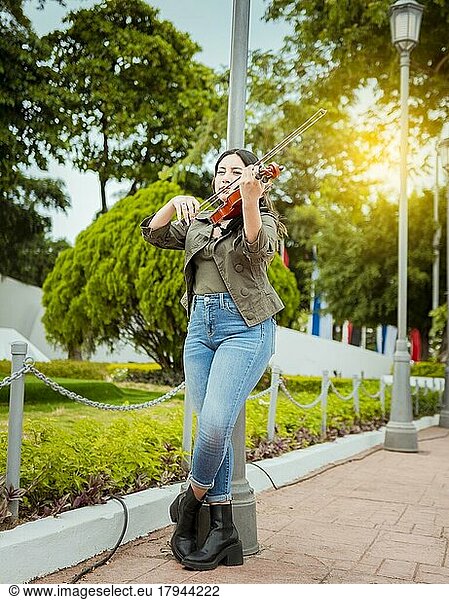 Woman playing violin in the street. Portrait of violinist girl playing in the street. Woman artist playing violin outdoors  Girl lying down playing violin in a park
