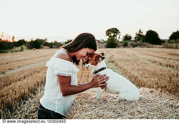 Woman playing with dog on straw bale during sunset