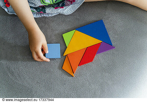 Woman playing with multi colored tangram on sofa