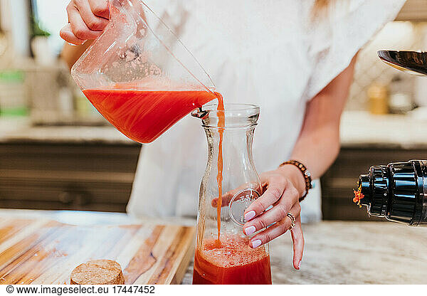 Woman pours freshly juiced fruits and vegetables into glass carafe