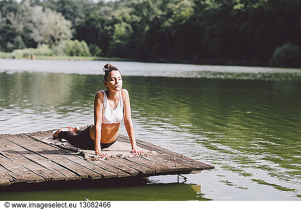 Woman practicing cobra pose on pier over lake in forest