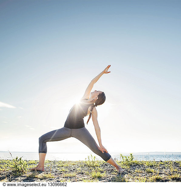 Woman practicing extended side angle pose yoga at beach during sunny day