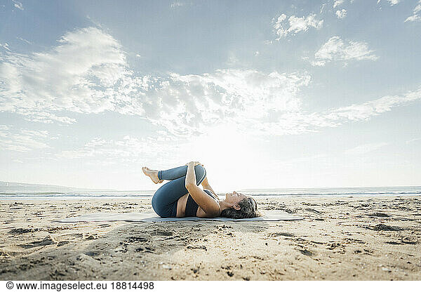 Woman practicing Pawanmuktasana lying down at beach