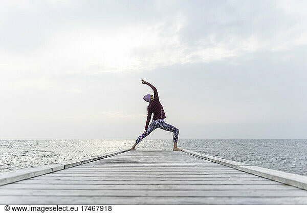 Woman practicing Utthita Parsvakonasana pose on pier