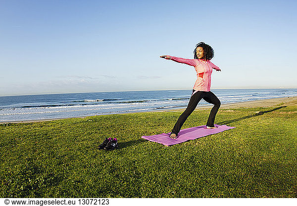 Woman practicing warrior 2 yoga pose on field against sea