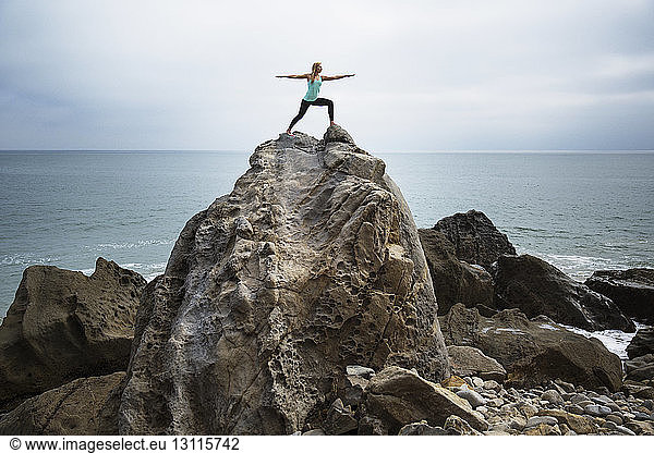 Woman practicing worrier 2 pose on rocks by sea
