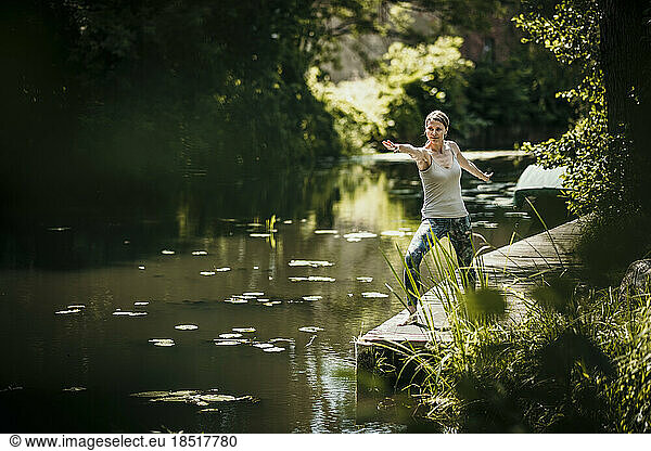 Woman practicing yoga on pier near lake
