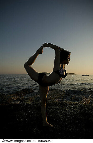Woman practicing yoga on the coast of Maine at sunset  New England.