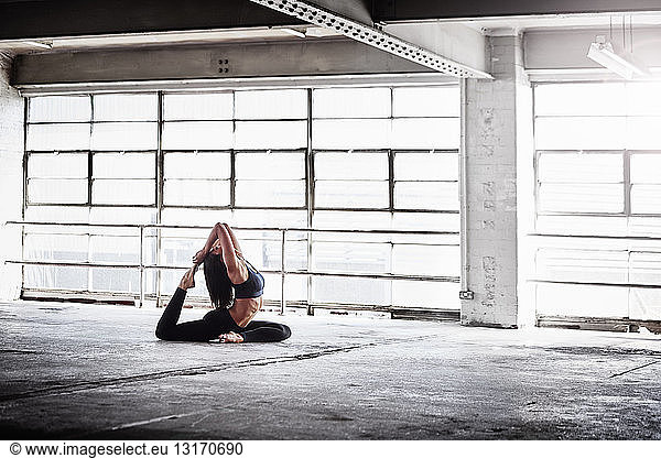 Woman practicing yoga pose in front of warehouse window